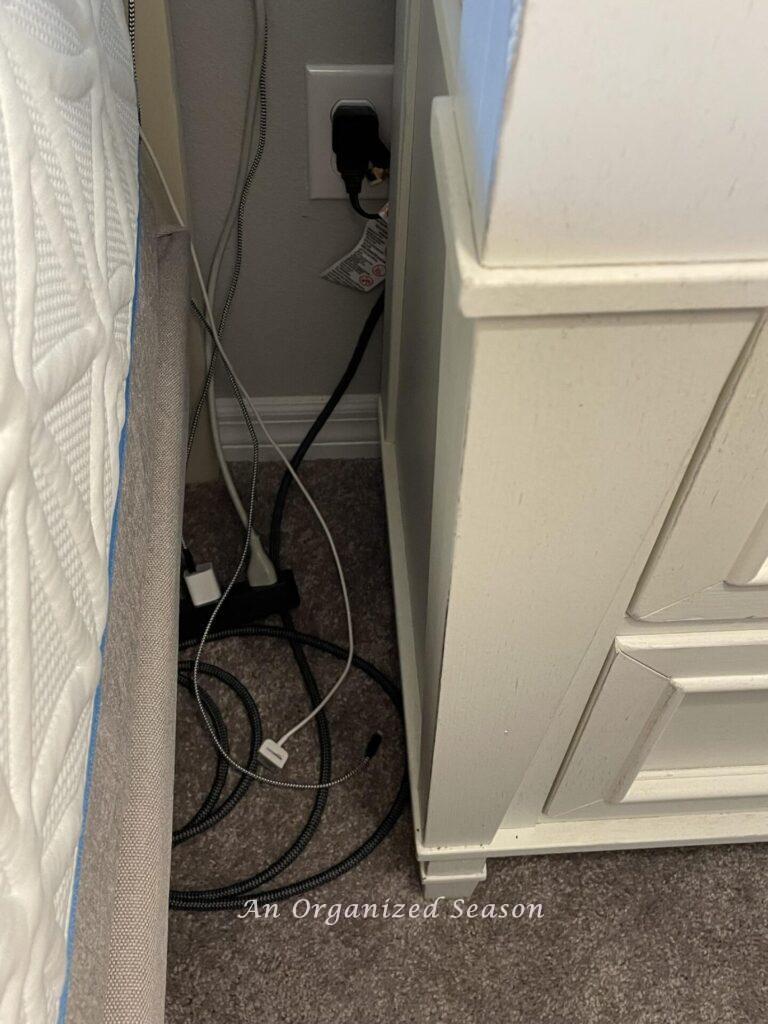 Messy cords between a bed and a nightstand. 