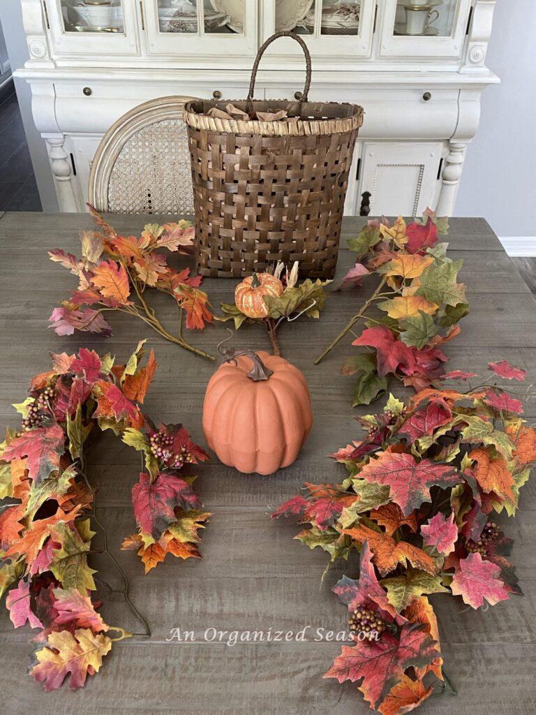 Gather four leaf stems, a basket, an orange pumpkin, and a pumpkin pick to make a Fall basket wreath for your front door. 