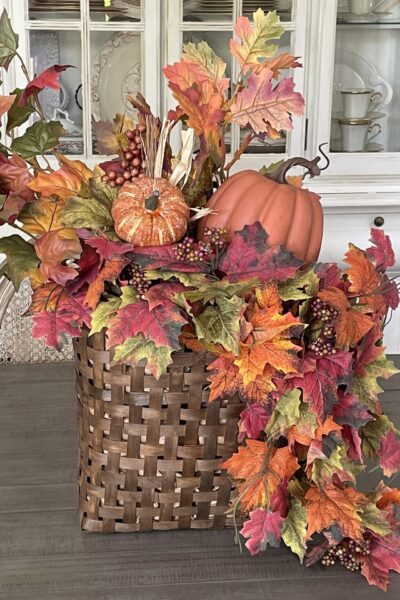 Basket wreath filled with fall leaves and two orange pumpkins.