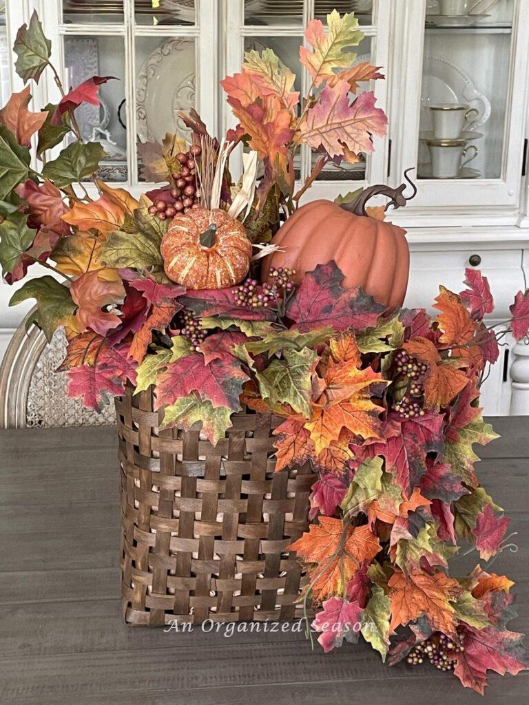 A basket filled with fall leaves and two pumpkins. 