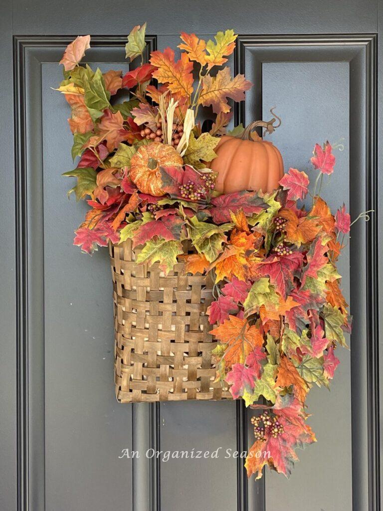 A fall basket with ;eaves and pumpkins hanging on a door. 