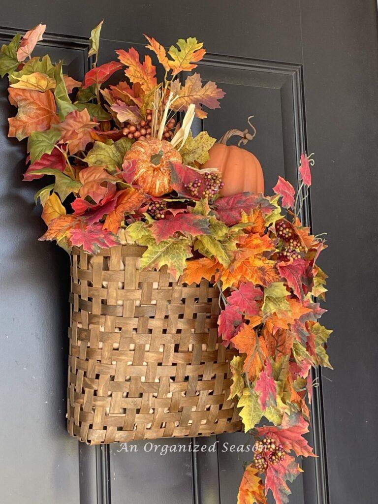 Left side view of a fall basket wreath hanging on a black door. 