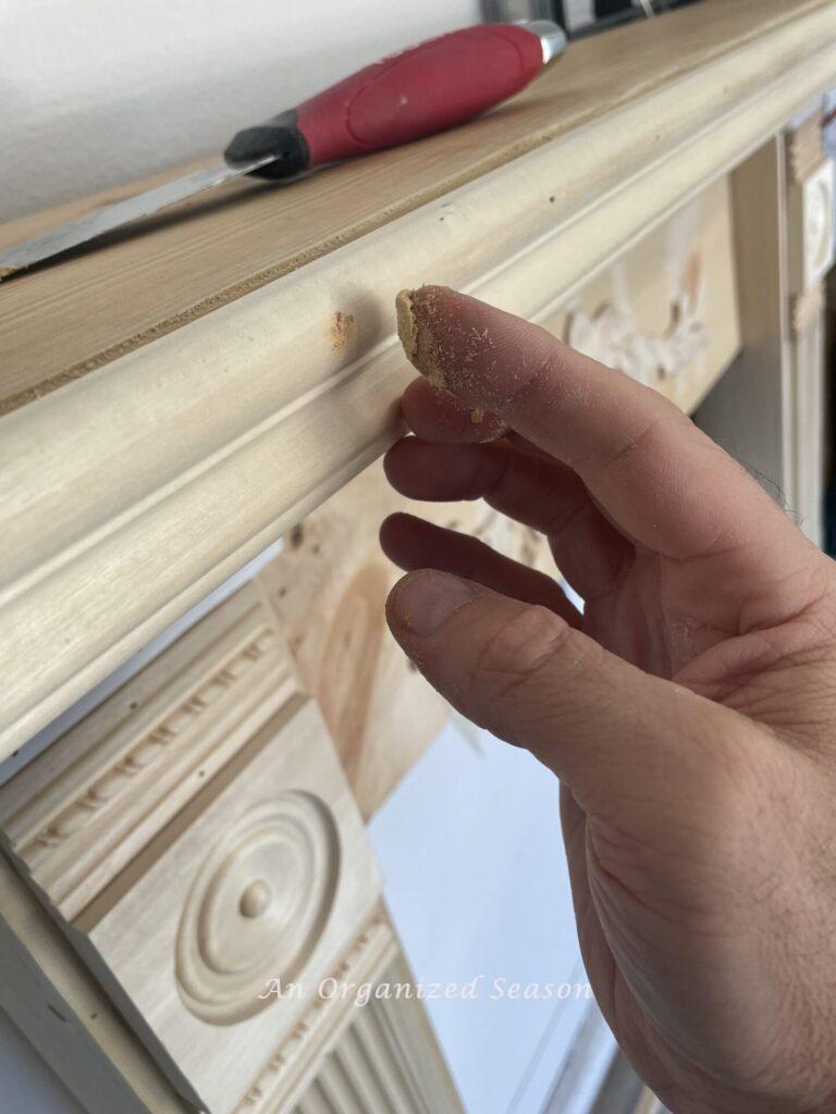 Hand putting wood filler on nail holes in decorative molding