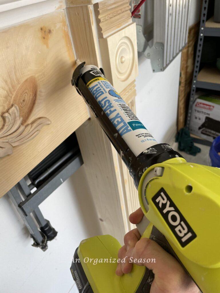 Hand holding caulk gun and applying caulk to mantel seams