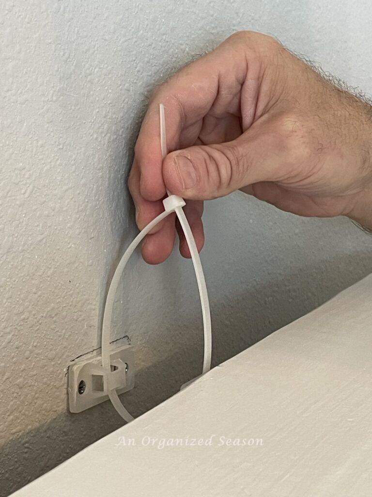 Hand holding zip tie before tightening to secure mantel to wall