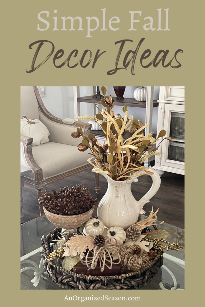 Fall vignette with pitcher of fall stems, wood bowl of pinecones, two pumpkin picks, and two twine pumpkins in a round basket tray. 