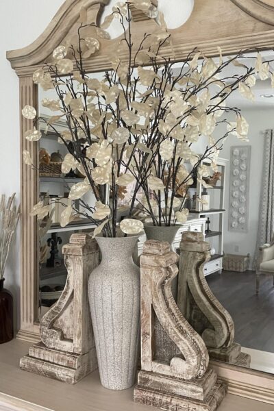 Neutral fall branches in a tall vase flanked by corbels.