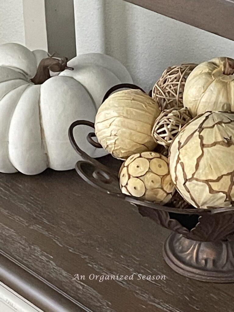 A white pumpkin next to a bowl of fall orbs. 