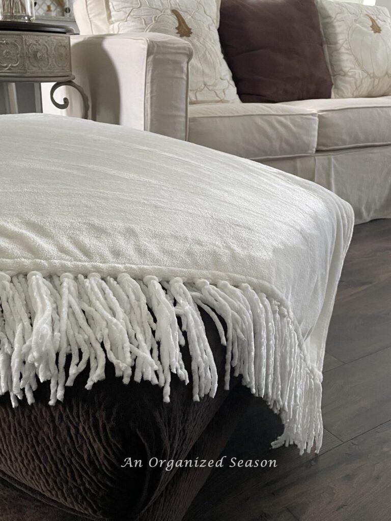 A white throw blanket covering the end of a chaise lounge. 