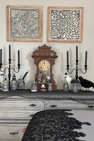 A dresser with antique clock, black candlesticks, a crow, and spooky potion bottles.