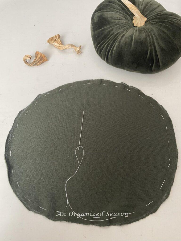 Step two to make DIY velvet pumpkins is to use a gathering stitch to sew thread 1/2' from the outside of the circle fabric. 