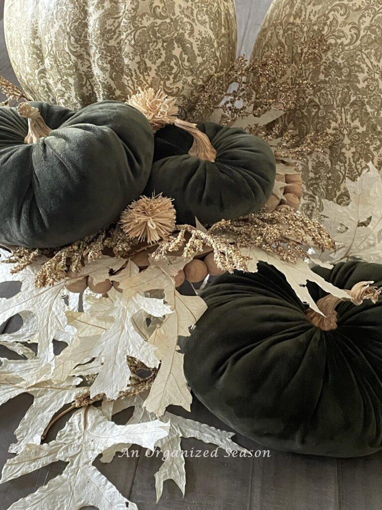Three green velvet pumpkins displayed with off white oak leaves. 