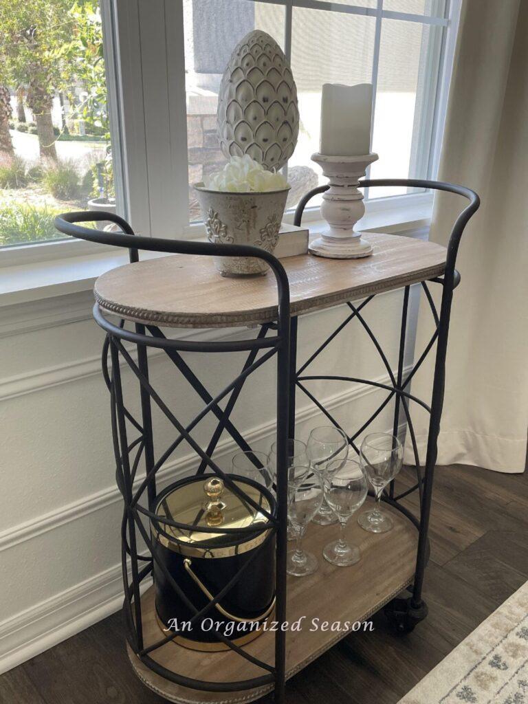 A metal bar cart with ice bucket, wine glasses, and three white decorative pieces.  