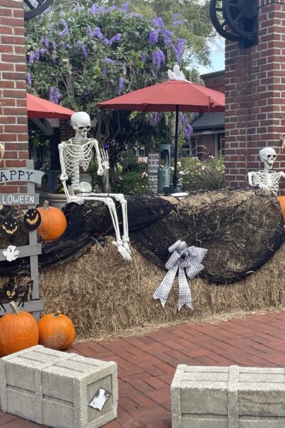 Skeletons sitting on hay bails with pumpkins.