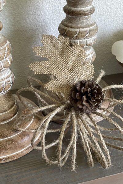 A jute twine pumpkin next to two candlesticks.