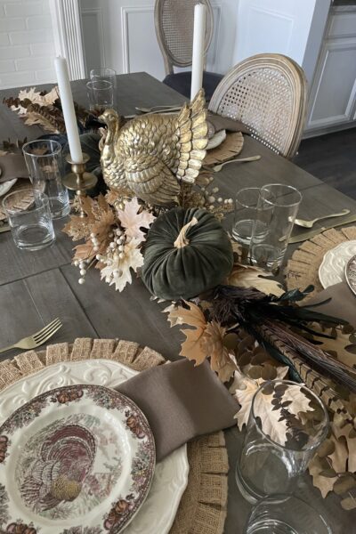 A Thanksgiving table with gold turkey, 2 candlesticks, green velvet pumpkin and organics.