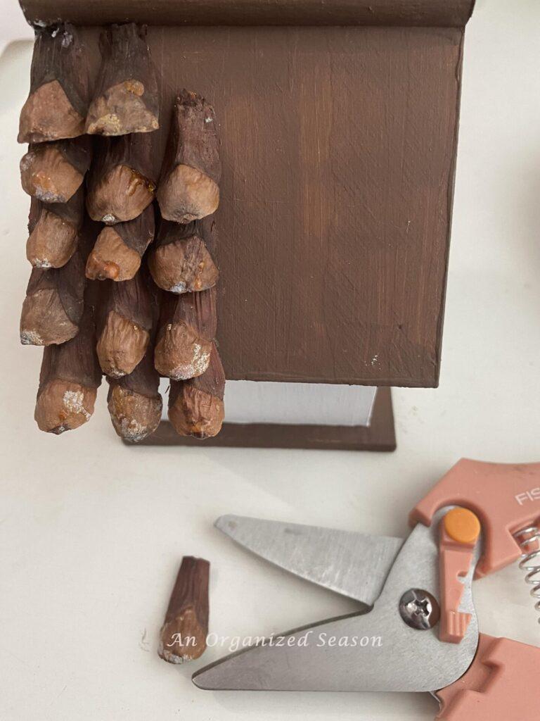 Pinecone pieces being glued onto a birdhouse roof. 