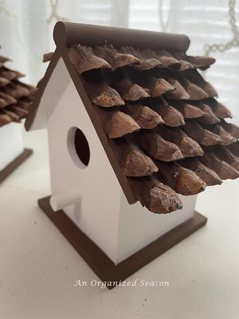 A birdhouse with pinecone pieces covering the roof.