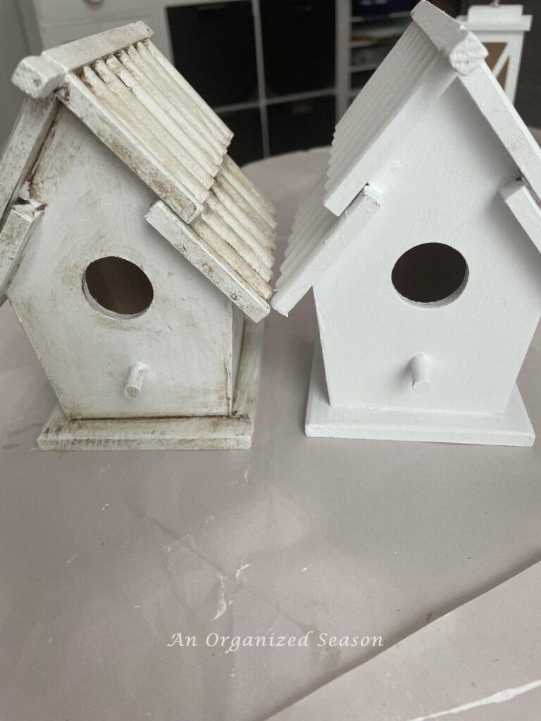 A white birdhouse next to an antiqued birdhouse. 