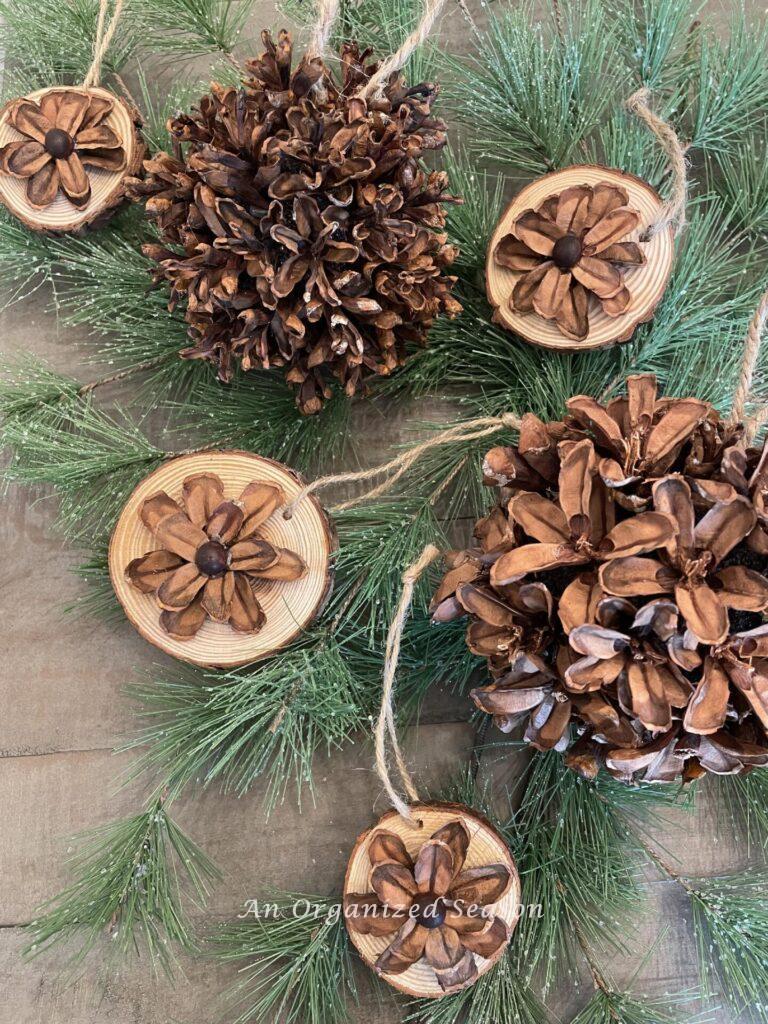 Pinecone and wood slice ornaments laying on greenery.