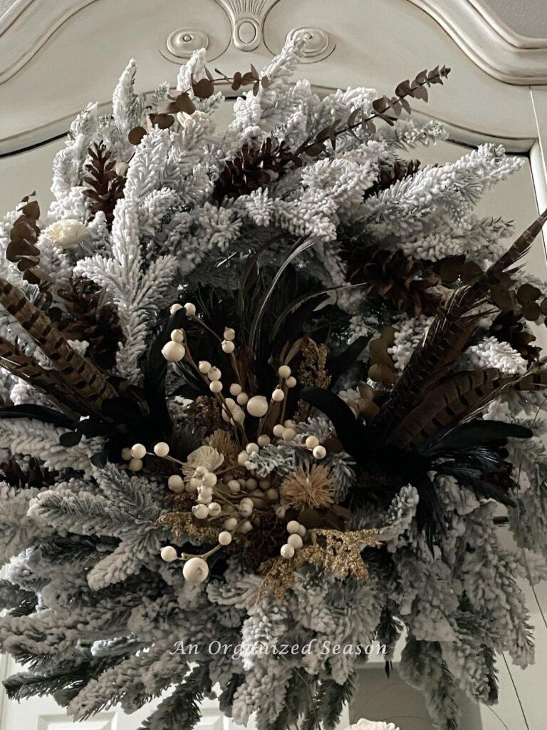 A flocked wreath decorated with feathers and neutral berries. 