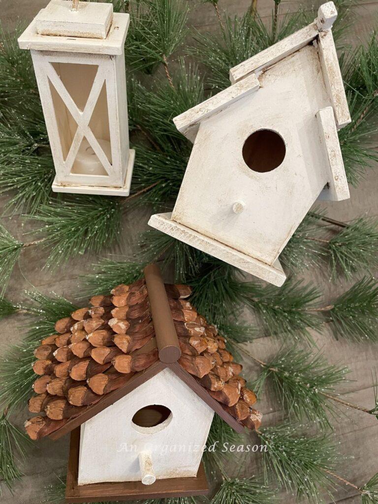 Two birdhouses and a lantern laying on greenery. 