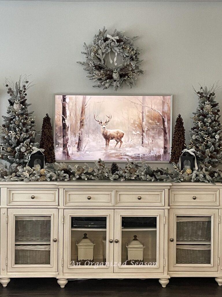 A deer picture on a frame TV with a console table under it that's decorated for Christmas. 