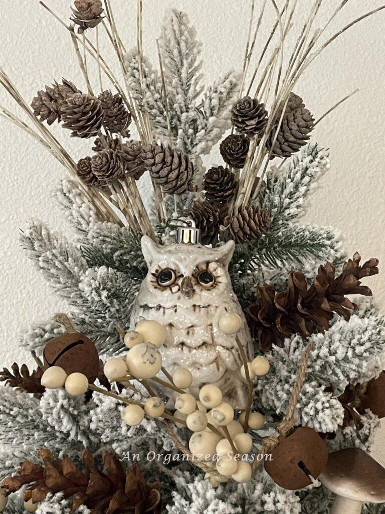 An owl and pinecone picks atop a Christmas tree.