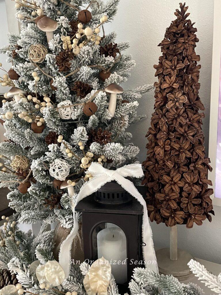 A pinecone Christmas tree next to a decorated evergreen tree and a lantern. 