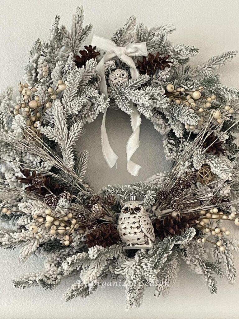 A wreath decorated with an owl, neutral berries, and pinecones. 