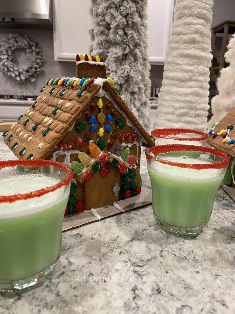 Cups of Grinch punch sitting by a gingerbread house.
