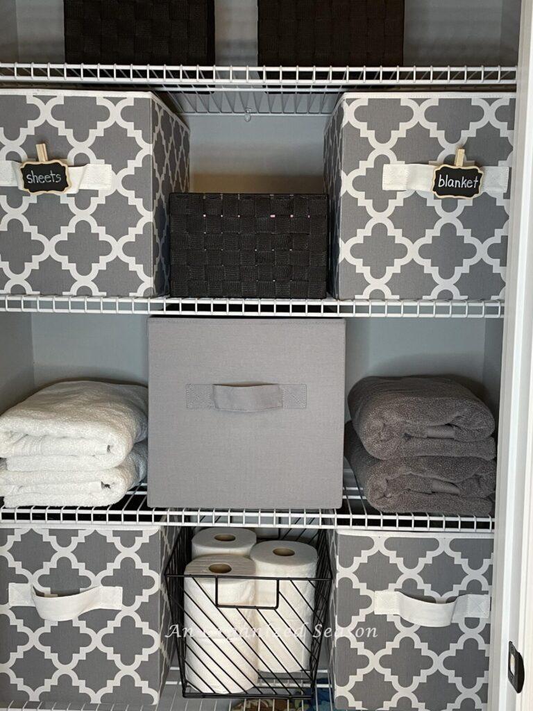 A bathroom closet organized with gray and white cube bins. 