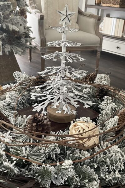 A white metal Christmas tree surrounded by an evergreen and grapevine wreath.