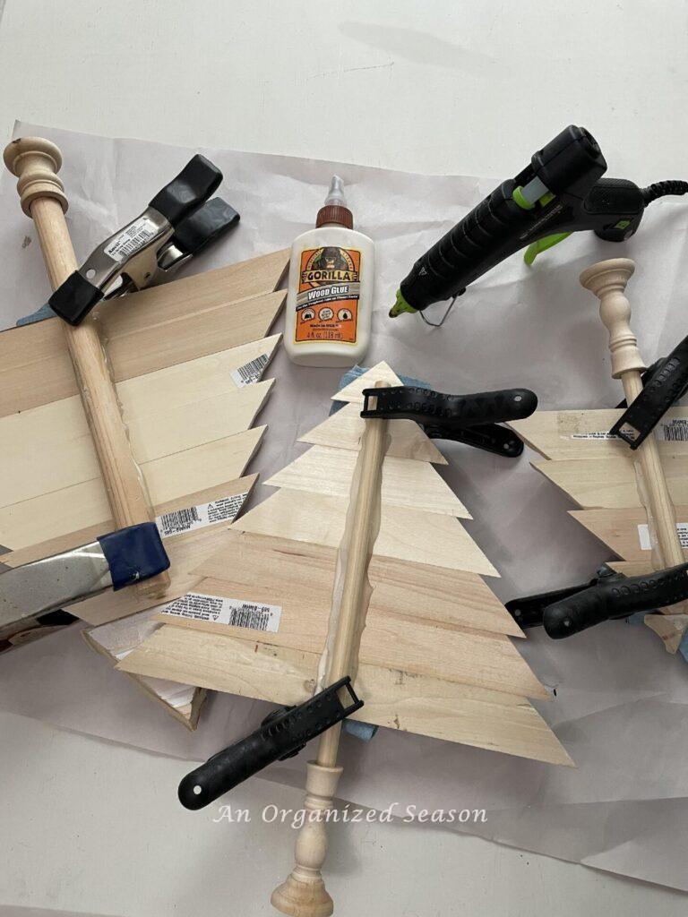 Step five to make a wooden Christmas tree is to glue the tree onto the dowel rod and hold with clamps. 
