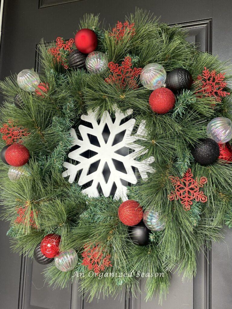 A wreath with snowflake in the center and round ornaments and smaller snowflakes make pretty Christmas porch decor. 