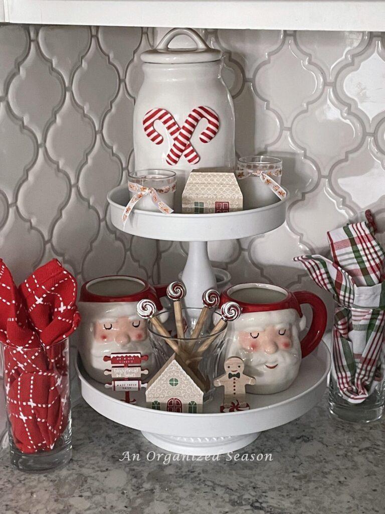 A tiered tray decorated with Santa mugs and gingerbread mini decor items. 