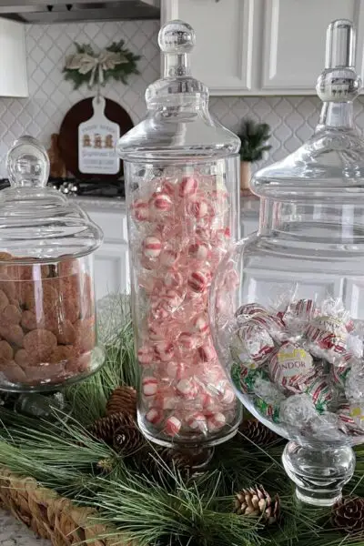 3apothecary jars filled with Christmas candy and cookies on a kitchen counter.