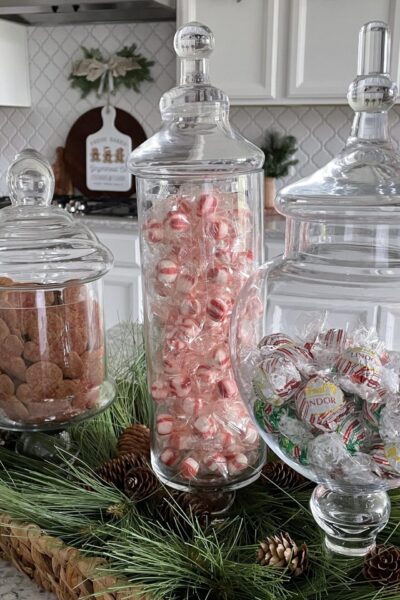 3apothecary jars filled with Christmas candy and cookies on a kitchen counter.