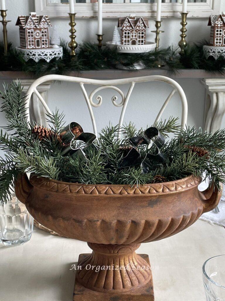 A centerpiece with an urn, evergreen stems and two gingerbread cookie cutters.