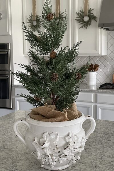 Small Christmas tree in a white vintage pot on a kitchen counter.