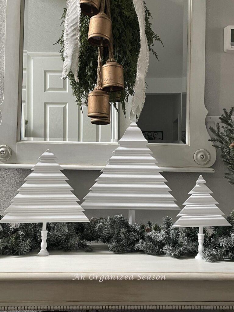 Three White wood Christmas trees on a foyer table. 
