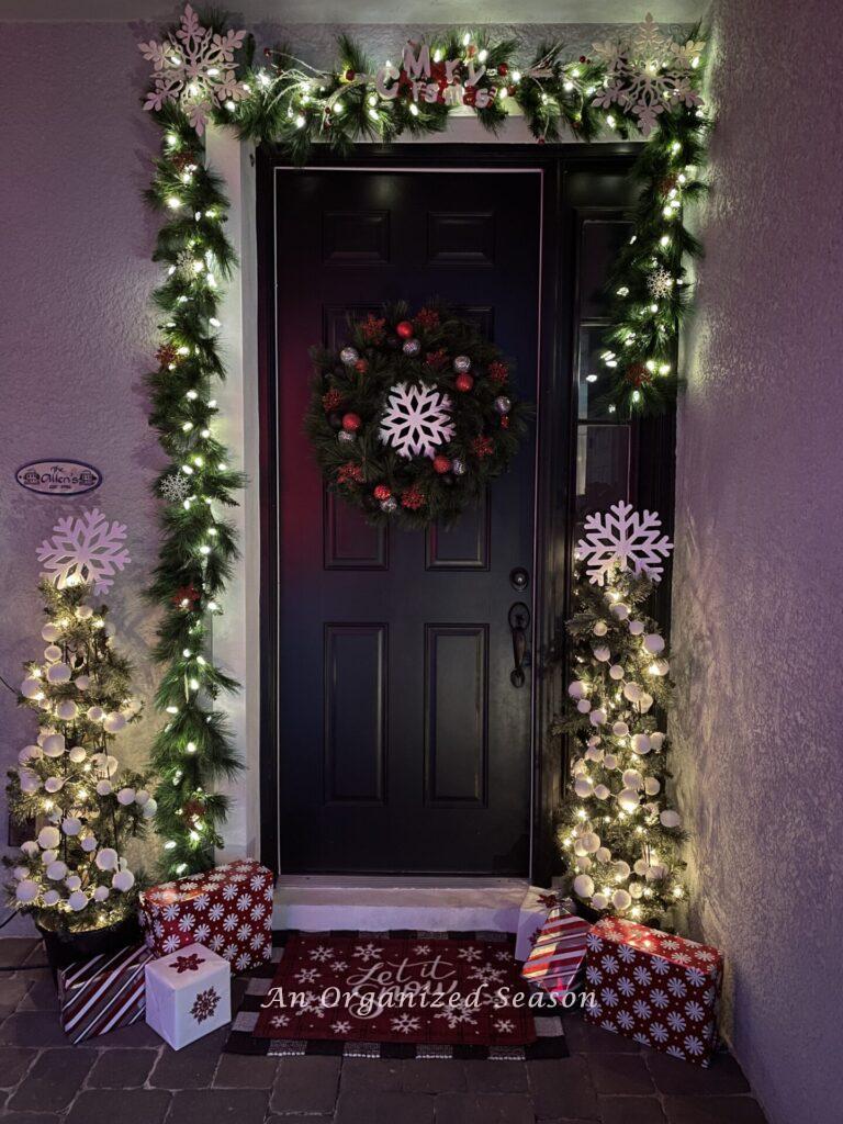 Porch decorated with garlands and lights welcoming guests to a Christmas home tour.