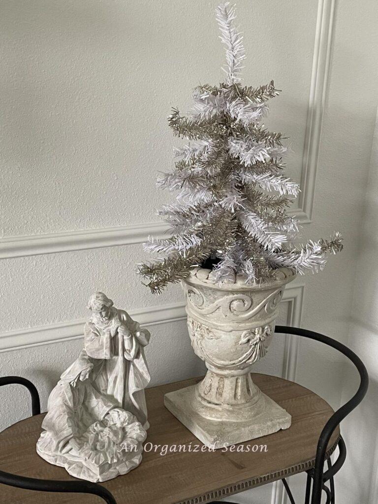 White tree in a cream urn next to a white statue of the holy family makes pretty neutral Christmas decor.
