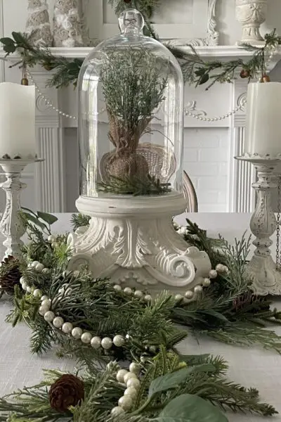Centerpiece with glass cloche on white pedestal and two white candles