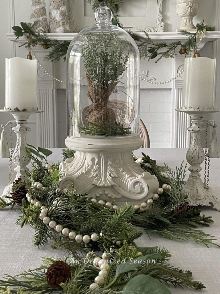 A centerpiece with a cloche on a pedestal with two white candlesticks on either side. 