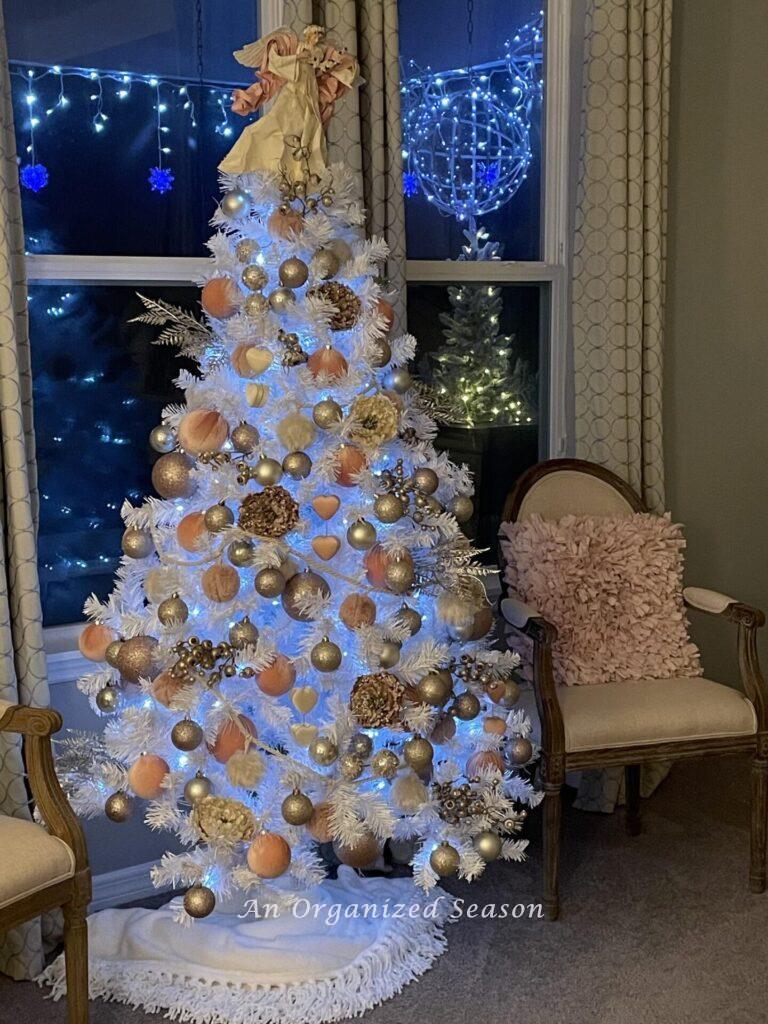 A white Christmas tree decorated with pink and champagne ornaments. 