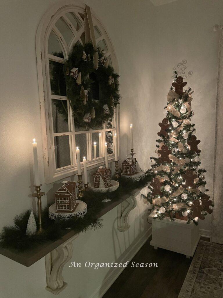 A gingerbread themed tree with white lights and candles on a shelf decorated with gingerbread houses. 