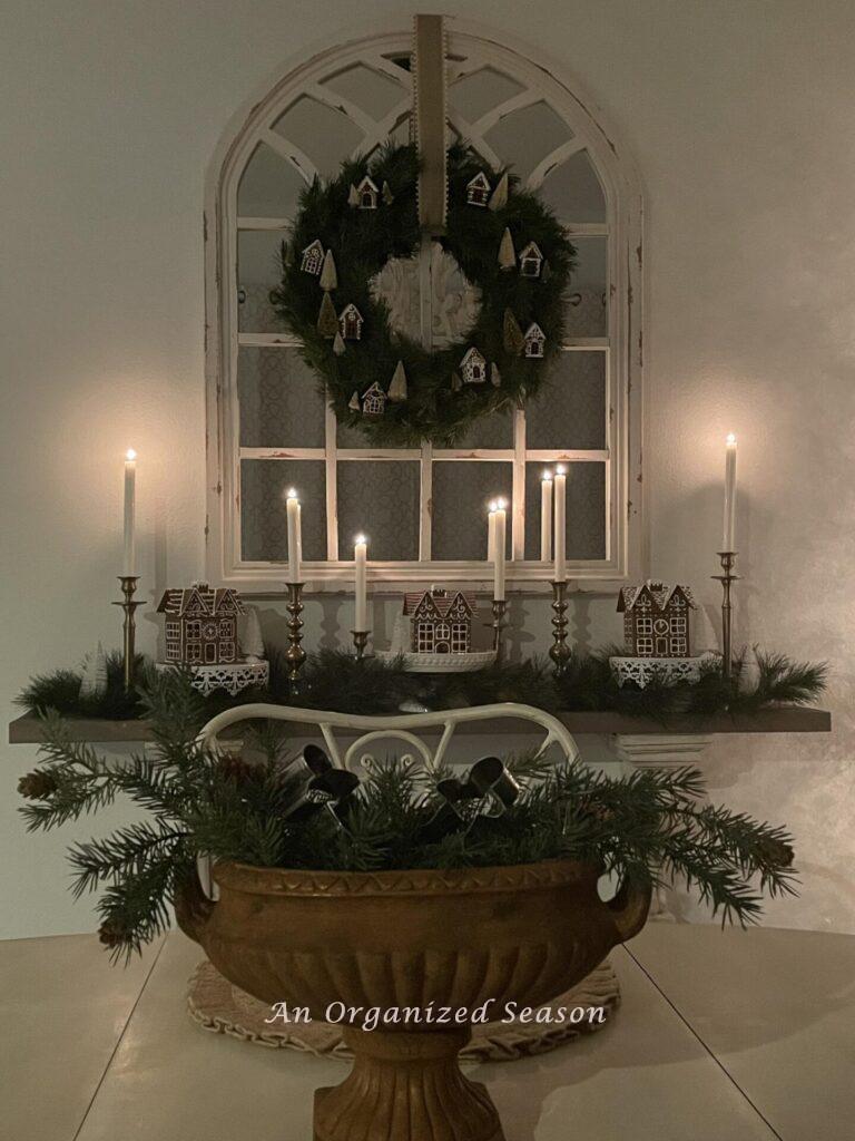 Six lit candles on a shelf with gingerbread houses with a wreath hanging above and decorated for a Christmas home tour.