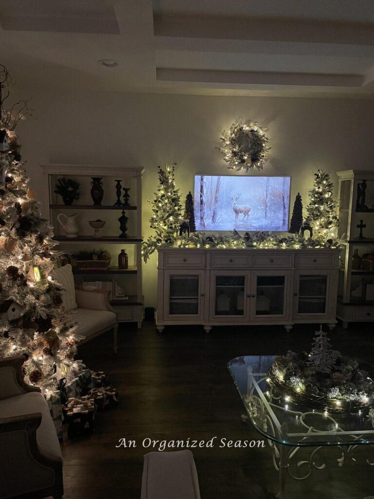 A living room with lit trees, wreath, and garland for a Christmas home tour.