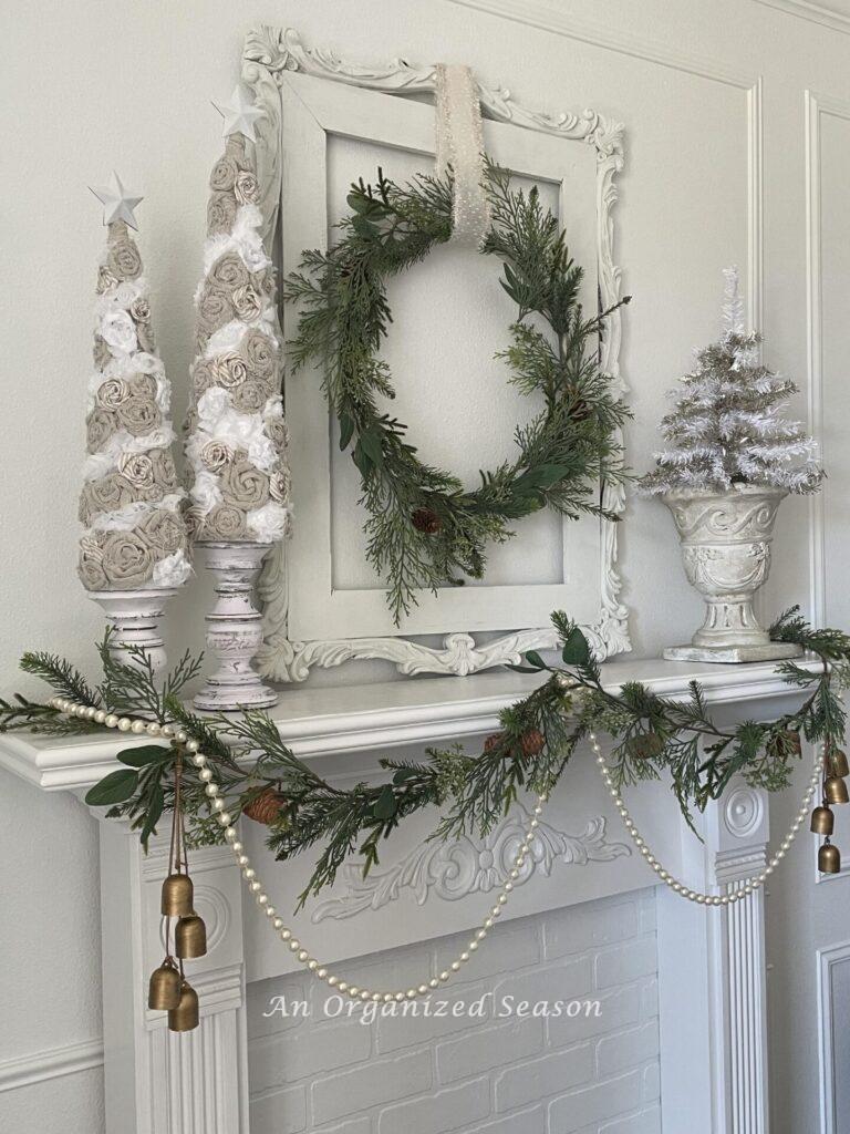A decorated mantel  with Christmas trees and a wreath. 